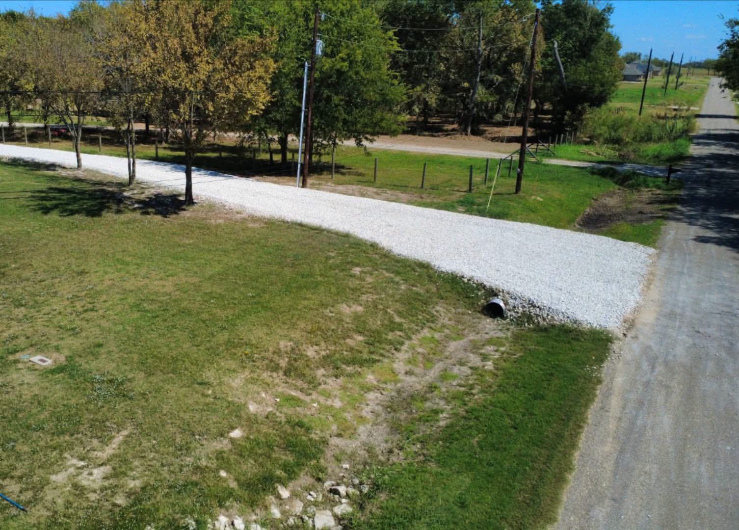 Aerial view of a completed gravel driveway leading to a rural property, with culvert pipe installed at the road