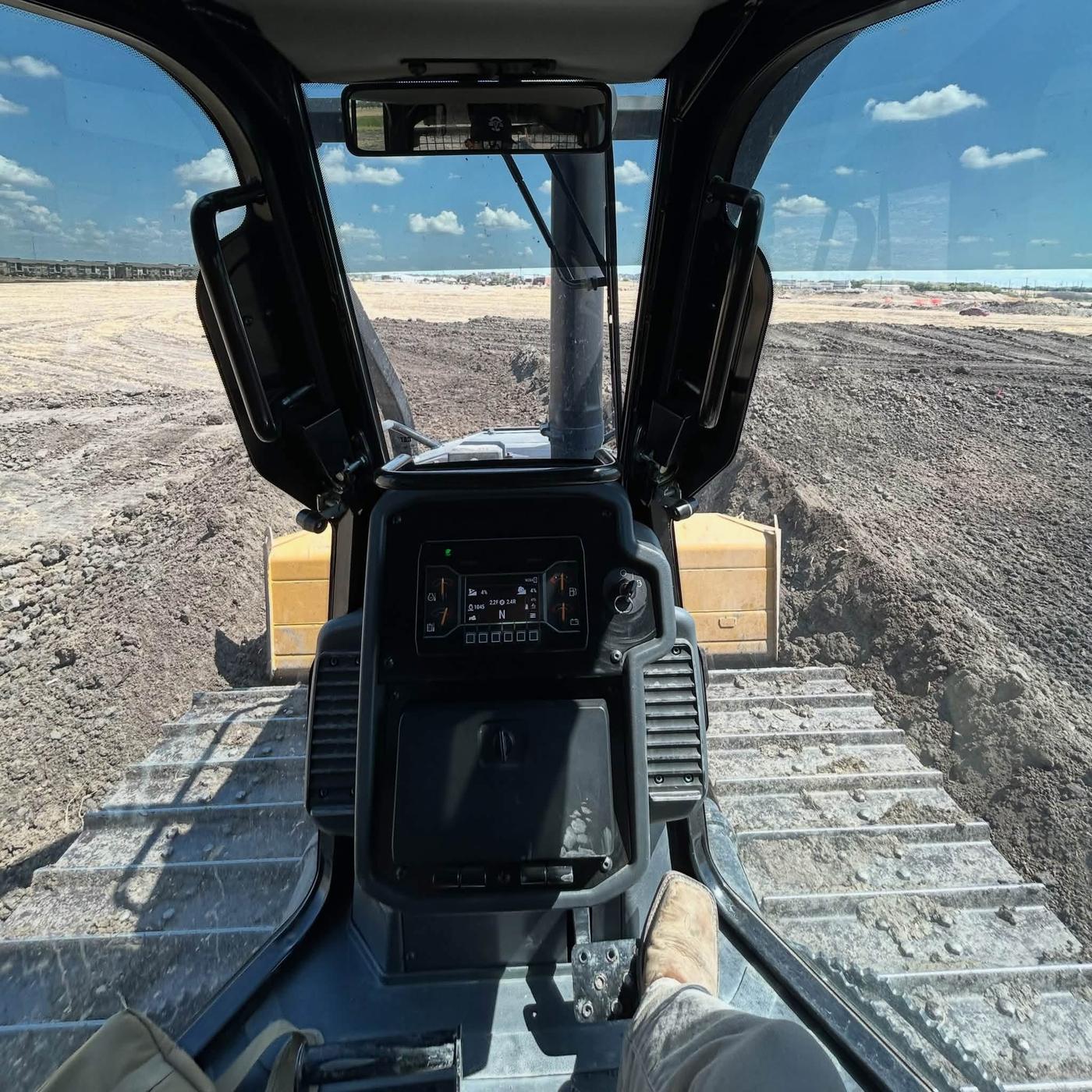 View from inside an excavator cab overlooking a large graded dirt site