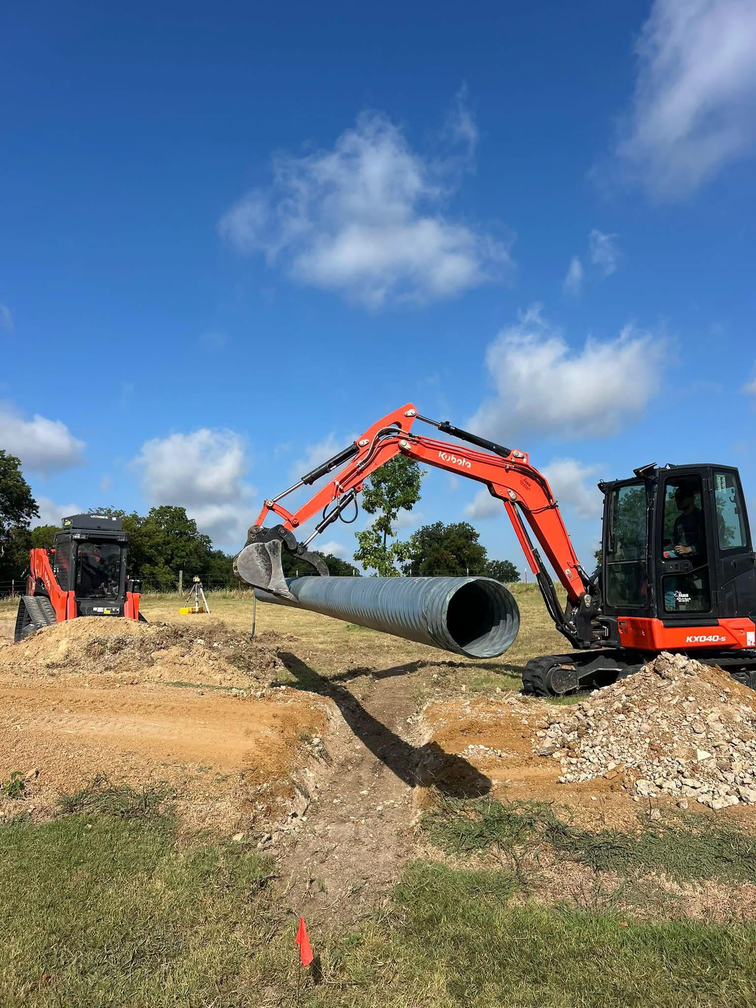 Excavator placing large culvert pipe into a trench during a dirt work project