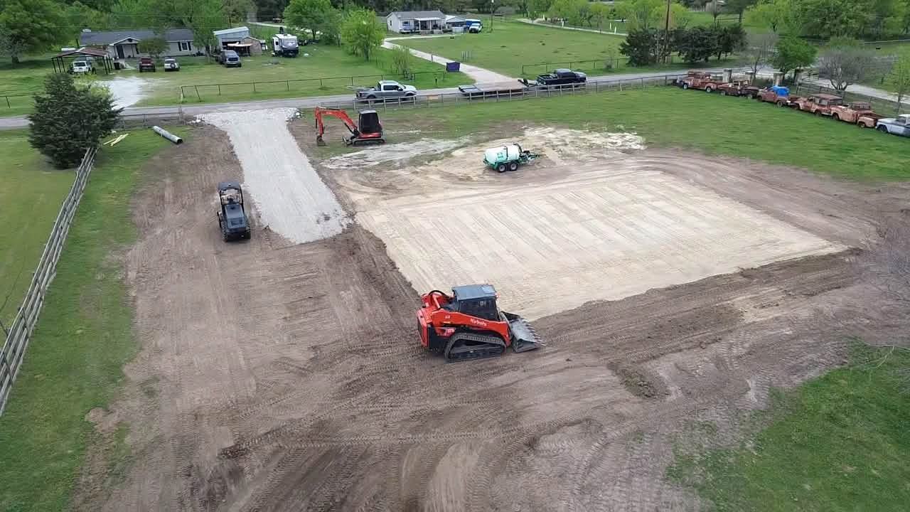 Aerial view of a large dirt site preparation project with excavator, skid steer, and water truck