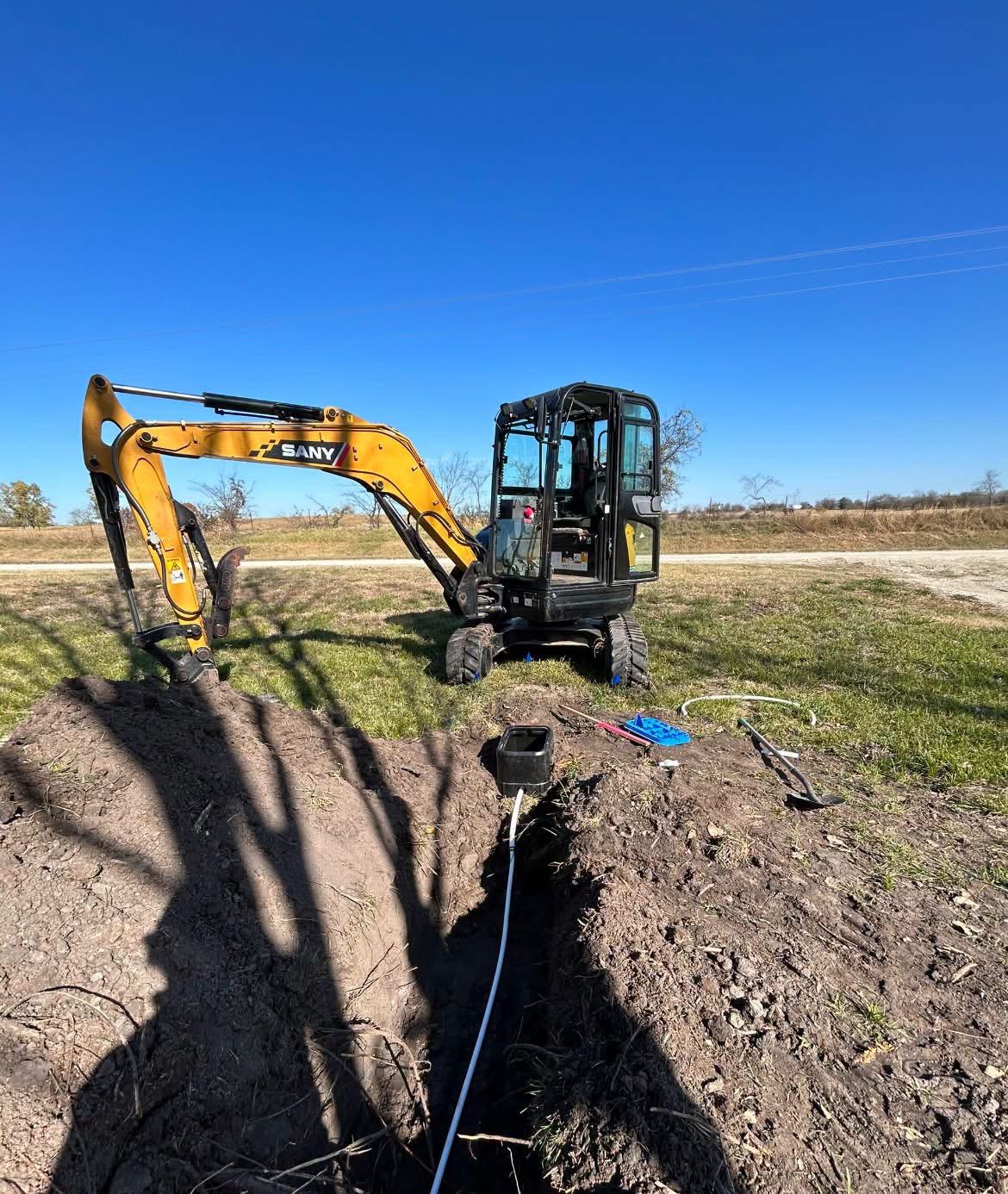 Mini excavator digging a trench along a rural driveway